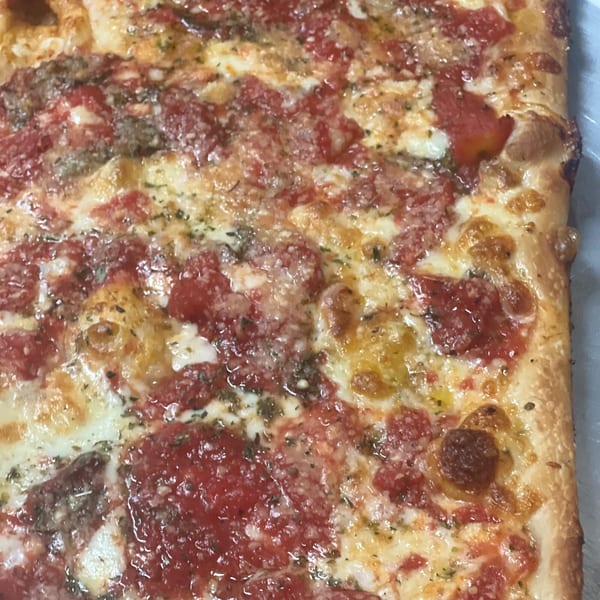 Close-up of a rectangular La Famiglia Pizza & Pasta pizza with cheese, tomato sauce, and herbs.