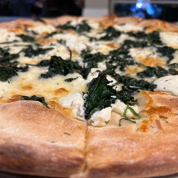 A close-up of a La Famiglia white pizza with spinach and ricotta cheese.