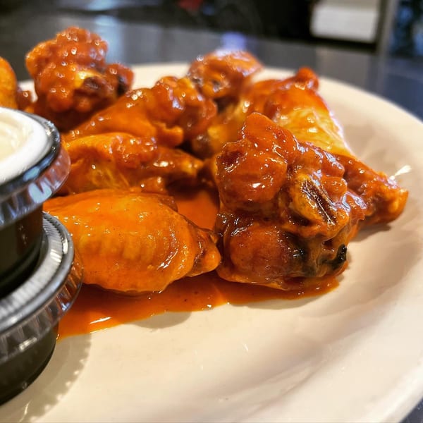 A close-up of La Famiglia's buffalo wings, glistening with orange sauce, served with a side of ranch.