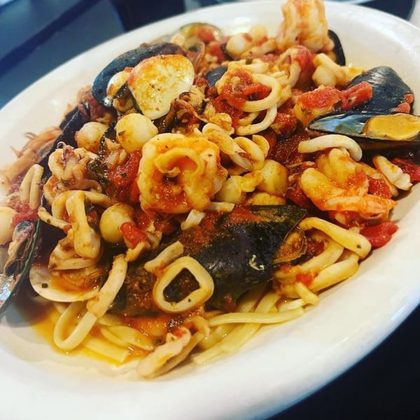A white bowl of La Famiglia's seafood pasta with mussels, scallops, shrimp, and calamari in red sauce.