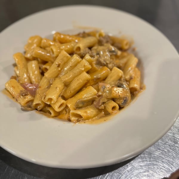 Rigatoni pasta with a creamy meat sauce and mushrooms on a white plate from La Famiglia.