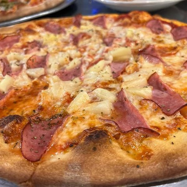 Close-up of a La Famiglia Hawaiian pizza with ham, pineapple, and melted cheese.
