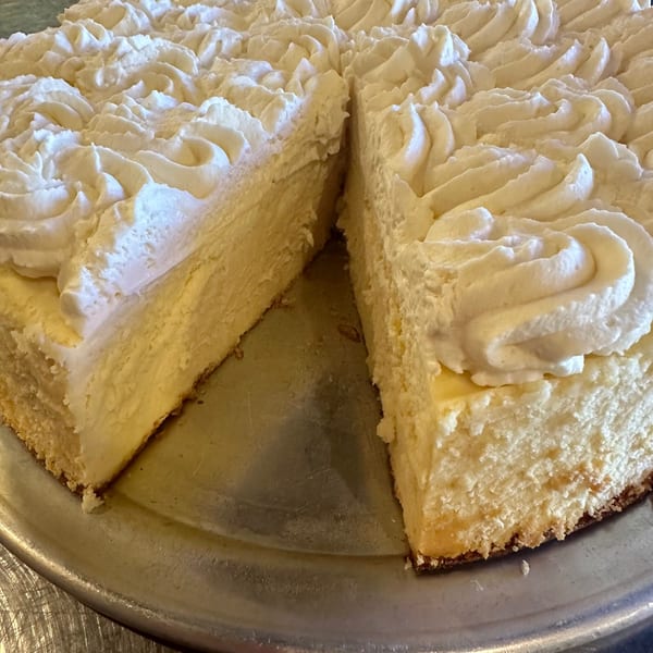 A large cheesecake with a slice removed, topped with swirls of white whipped cream.