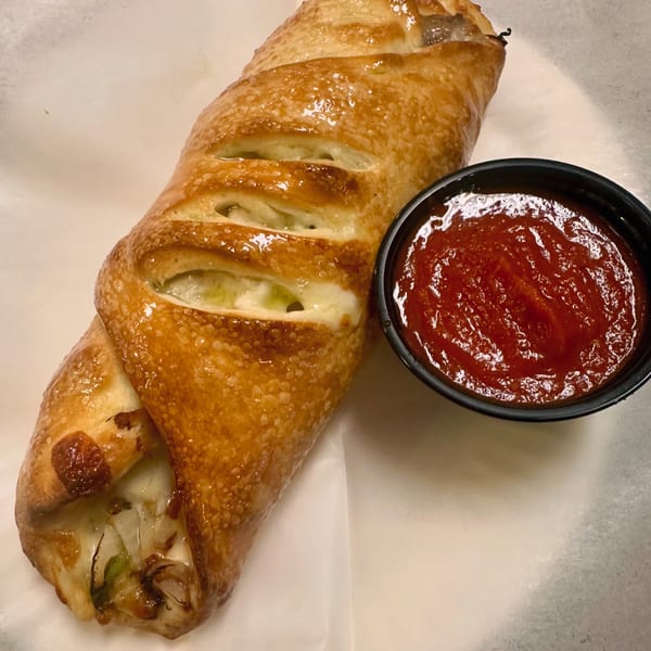 A golden-brown calzone with visible cheese and vegetables, served with a side of red marinara sauce.