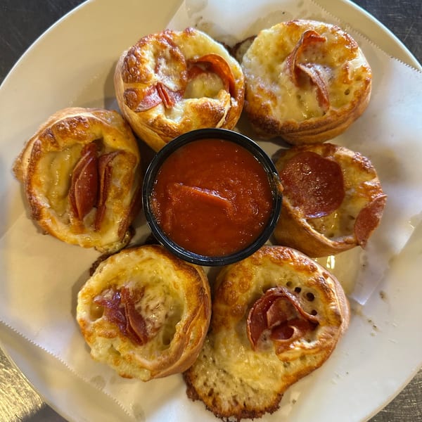 Six mini pepperoni pizza cups with melted cheese and a side of marinara sauce.