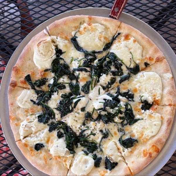 La Famiglia Pizza & Pasta's white pizza with ricotta cheese and spinach, sliced on a metal pan.