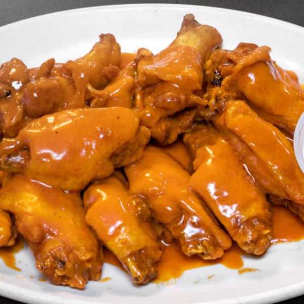 A white plate piled high with La Famiglia's buffalo wings, coated in a vibrant orange sauce.