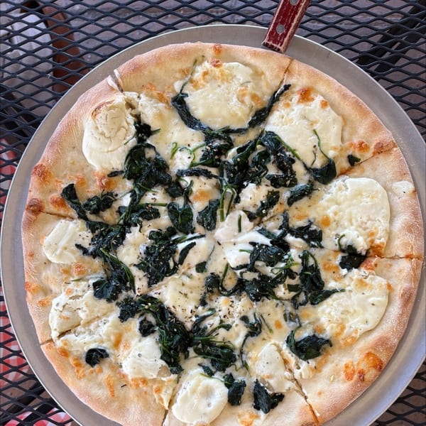 La Famiglia's white pizza with ricotta cheese and spinach, sliced on a metal pan.