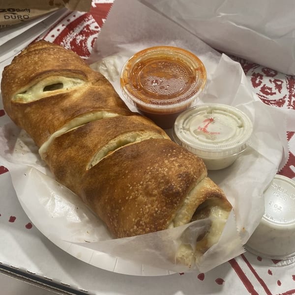 A golden-brown La Famiglia stromboli with melted cheese, served with marinara and ranch dipping sauces.
